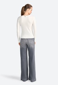 Top a maniche lunghe a coste color crema con scollatura tonda e piccolo dettaglio a bottone sul retro, abbinato a jeans in denim grigio sbiadito e dal taglio morbido.