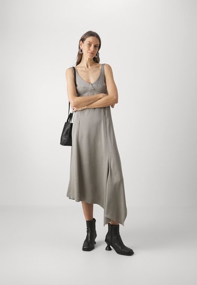 Mouwloze, grijze zijden jurk met een asymmetrische zoom, gecombineerd met zwarte enkellaarsjes en een kleine zwarte handtas. Gladde textuur, casual ontwerp.