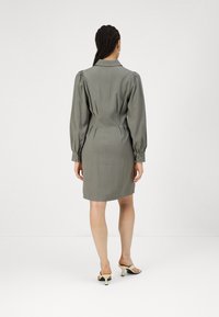 Rochie ajustată dintr-un material verde măsliniu, cu mâneci bufante, guler și o siluetă ajustată, prevăzută cu cusături pe spate și manșete cu nasturi.