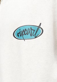 Valge kangas, millel on ümmargune sinine logo musta tekstiga, stiliseeritud kui "ripcurl", ja dekoratiivne alljoon.