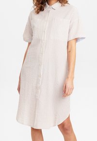 Gestreiftes Button-Down-Kleid in Beige und Weiß, mit kurzen Ärmeln, einem Kragen, zwei Brusttaschen und einem abgerundeten Saum. Strukturierter Stoff.