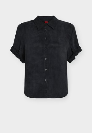 Chemise noire à manches courtes boutonnée avec poignets pliés et col pointu, présentée sur un fond clair uni.