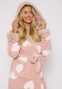 Bata de baño rosa con capucha hecha de un tejido suave y esponjoso, con grandes estampados de corazones blancos y un lazo en la cintura con bolsillos laterales.