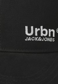 Črna kapa z izvezenim logotipom "Urbn JACK&JONES" v beli barvi. Tkanina ima teksturiran zaključek z vidnimi šivi.