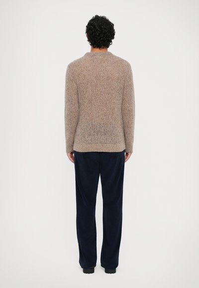 Vaalean beige neulepusero, jossa on teksturoitu pinta, pyöreä pääntie ja pitkät hihat. Yhdistetty tummansinisiin corduroy-housuihin, katsottuna takaa.