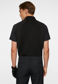 Svart polo skjorta med en texturerad bakpanel, korta ärmar och en diskret logotyp. Matcher med mörka byxor och en svart handske.