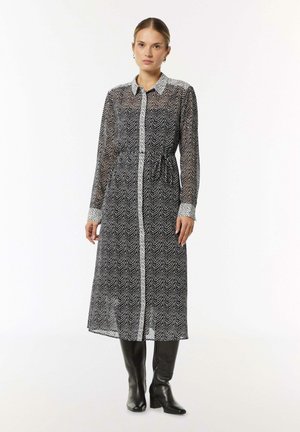 Black and white, long-sleeve, patterned dress with a collared neckline, button front, elastic waist, and smooth fabric, paired with knee-high black boots.