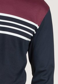 Long-sleeve shirt with a maroon upper portion and navy lower part, featuring three white horizontal stripes on the chest area.