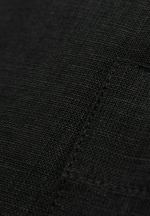 Czarna tkanina o teksturowanej fakturze z tkanym wzorem, z widocznym szwem i konturem kieszeni, emanująca subtelnym i trwałym wyglądem.