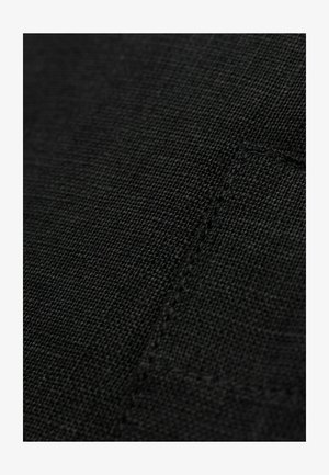 Černá texturovaná tkanina s tkaným vzorem, která má viditelné švy a obrys kapsy, vyjadřující jemný a odolný vzhled.