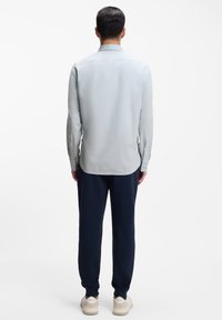 Φωτεινό γαλάζιο πουκάμισο με μακριά μανίκια και γιακά με κουμπιά, σε συνδυασμό με σκούρο μπλε αθλητικό παντελόνι και παπούτσια σε ουδέτερες αποχρώσεις, από πίσω όψη.