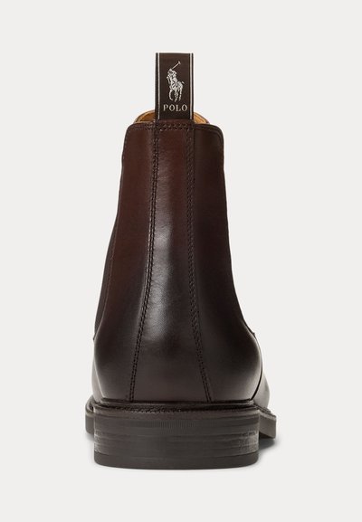 Botas de cano curto em pele castanha com acabamento liso, apresentando uma tira preta para puxar com um logótipo e um salto empilhado para maior estabilidade.