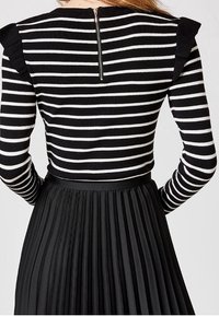 Svart- och vitrandig topp med långa ärmar, med axelrufflor och dragkedja i ryggen. Åtföljd av en svart plisserad kjol.