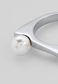 Bracciale d'argento con design triangolare, caratterizzato da un'accente in perla bianca liscia a un'estremità, finitura metallica lucida, stile minimalista.