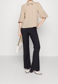 Beige blus med kort ärm och krage, kombinerad med svarta utsvängda byxor. Vit vadderad handväska med guldkedja, och krämfärgade klackskor med blockklack.