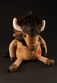 Plush bison toy with brown and tan fur, black horns, and embroidered red maple leaf. Soft texture; short limbs and a rounded body shape.