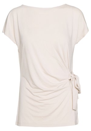 Vaaleanbeige lyhythihainen pusero pehmeää puuvillaa, jossa on pyöreä pääntie, laskostettu etuosa ja sivusolki, joka luo istuvan ilmeen.