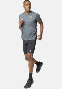 Grijze sport-T-shirt met korte mouwen, zwarte compressiekorte broek en zwarte hardloopschoenen. Heeft een logo op het T-shirt en de broek.