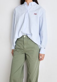 Světle modrá košile na knoflíky s límečkem, s malým červeným logem "Tommy". V kombinaci se zelenými volnými kalhotami. Hladká textilní struktura.