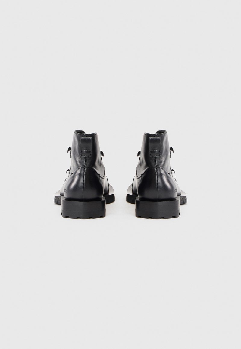 Ein Paar schwarze Lederstiefeletten mit dicken Profilsohlen, von hinten auf einem schlichten weißen Hintergrund gezeigt.