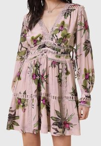 Robe fleurie rose clair avec manches longues, détails en dentelle, et un décolleté en V profond portée par une personne aux cheveux foncés et un petit collier.