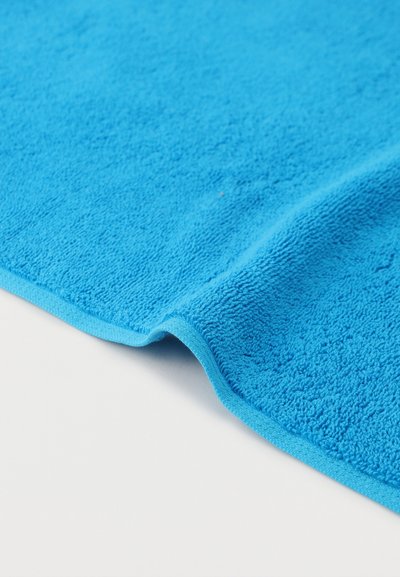 Serviette en éponge bleu vif avec bord plié sur une surface blanche, mettant en valeur la texture et la douceur du tissu.