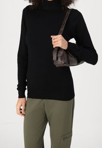Black turtleneck sweater in a soft material with ribbed cuffs and hem; paired with olive green pants and a small dark leather shoulder bag.