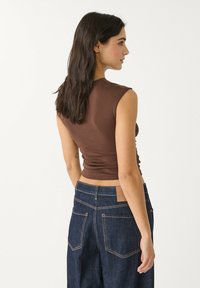 Brun, figursydd ärmlös topp som matchas med högmidjade, mörkblå jeans i denim med synliga sömmar och ett märke på baksidan.