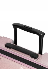 Coperchio di valigia rigida rosa glitterato con manico telescopico nero e pulsante. Presenta una cerniera nera e una striscia di accento.