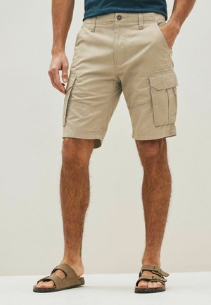 Beige cargo shorts med sidelommer, lavet af bomuld, med lige pasform og lynlås, parret med brune sandaler.
