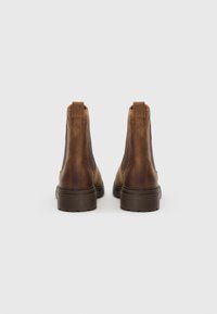 Bottes chevilles en cuir marron avec des panneaux latéraux élastiques, une tige texturée et des semelles en caoutchouc épaisses. Elles possèdent une languette en boucle au niveau du talon pour un enfilage facile.