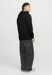 Sudadera negra con capucha y mangas largas, de tela suave y con puños de canalé, combinada con unos vaqueros oscuros de corte holgado y zapato tipo sneaker blanco.
