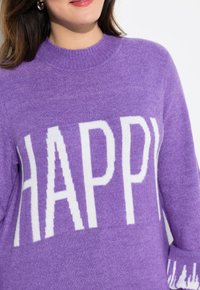 Lila Pullover mit weicher Textur, der auffällige weiße "HAPPY"-Schriftzug auf der Brust und einen gerippten Rundhalsausschnitt aufweist.