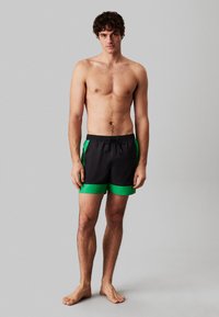 Czarne kąpielówki z zielonymi akcentami, z elastycznym pasem ze sznurkiem, w jednolitym kolorze i sportowym designie. Idealne na casualowy strój plażowy.