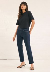 Top negro de manga corta combinado con jeans ajustados de color azul oscuro que cuentan con bolsillos frontales y costuras en contraste, complementado con sandalias de tacón negras.