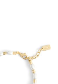 Bracelet en chaîne dorée présentant des perles blanches ovales et un fermoir à homard. Comprend une étiquette portant la gravure "COACH."