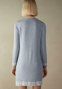 Ljust blå långärmad klänning i mjukt material, med spetsdetaljer vid ärmar och fåll, enkel rund halsringning och len yta.