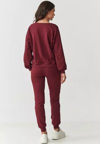 Bordowy sweatshirt i dopasowane spodnie dresowe wykonane z miękkiej tkaniny; charakteryzują się ściągaczami na mankietach i w pasie, oferują luźny krój oraz gładką teksturę.