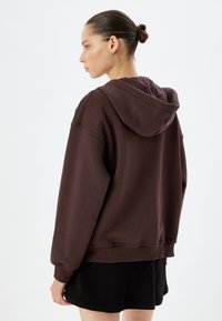 Felpa marrone con una vestibilità comoda, dotata di un ampio cappuccio, maniche lunghe e polsini a coste, abbinata a una gonna nera. Design semplice, texture morbida.