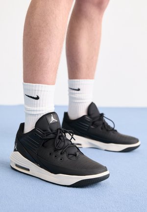 Jalat, joissa on valkoiset Nike-sukat ja mustat Air Jordan -lenkkarit, seisovat vaaleansinisellä pinnalla valkoista taustaa vasten.