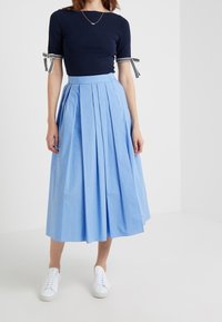 Navy fitted top with striped sleeves paired with a light blue, pleated midi skirt and white sneakers. Smooth fabric and relaxed fit.