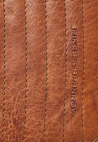 Brunt læderoverflade med lodrette syninger og præget tekst "SPIKES & SPARROW" på højre side.