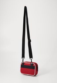 Rote Tasche mit schwarzem Tragegurt und Akzenten. Verfügt über eine strukturierte Oberfläche, einen Reißverschluss und kontrastierende Paspelierung. Kompakte rechteckige Form.