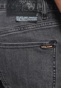 Vaqueros de mezclilla negra con un parche trasero texturizado que presenta un emblema, detalles de costura y un pequeño logo de Volcom acentuado en el bolsillo.