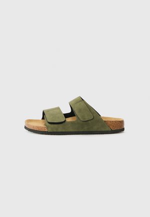Sandal in suede verde con due cinturini regolabili, soletta in sughero e suola in gomma nera. Presenta una suola piatta e un design minimalista.