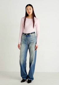 Un haut rose clair à manches longues associé à un jean bleu délavé à coupe ample avec un dégradé de couleur ; comprend une ceinture noire et des chaussures noires à bouts pointus.