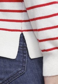 Rood-witte gestreepte trui van rib gebreid materiaal, met een gespleten zoom en aansluitende mouwen, gecombineerd met donkerblauwe denim.
