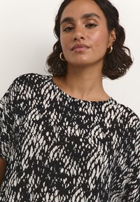Black and white patterned top with a loose fit, round neckline, and short sleeves. The texture appears soft with a flowing design.