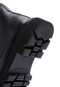 Stivale in pelle nera con suola inferiore robusta, caratterizzata da motivi di grip testurizzati e un tallone rinforzato. Design semplice, adatto a diversi terreni.