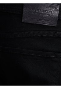 Jeans en denim noir montrant la poche arrière et une étiquette en cuir cousue avec la marque "JACK & JONES JEANS INTELLIGENCE".